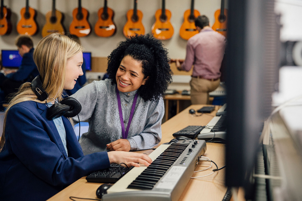 Student in a school playing a keyboard, with her teacher sat next to her.